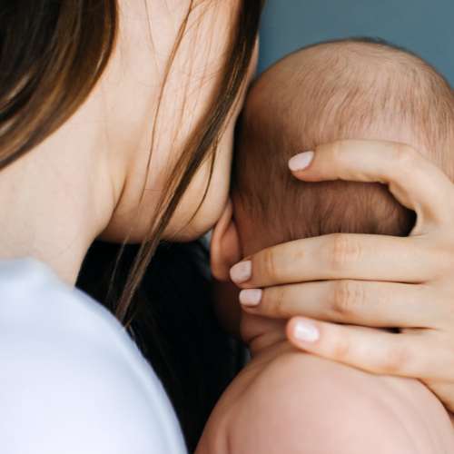 A lady holding her baby after receiving postnatal reflexology treatment